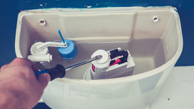 person with a screwdriver working on the tank of a toilet