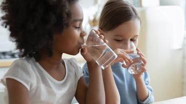 two children drinking water from a glass
