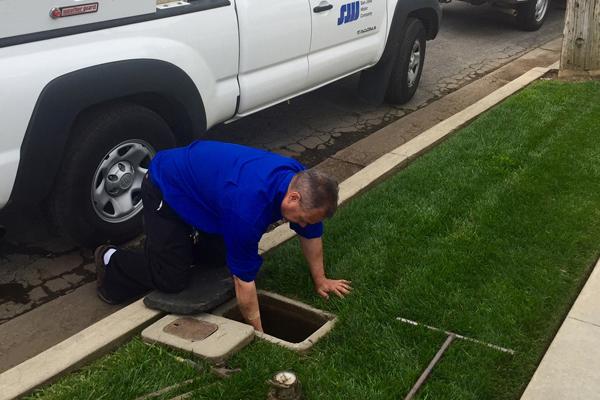 Man kneeling down to reach into a water service access point near the curb